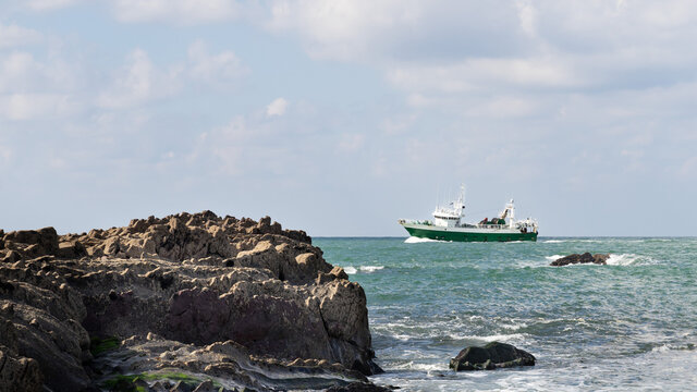 A traditional fishing boat fishing near the shore. There are rocks on the shore