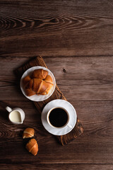 A cup of coffee and croissants on a dark wooden background. Free space for signature.