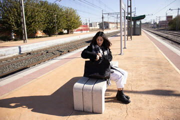 young brunette woman next to railroad arden with luggage, waiting for passenger train.