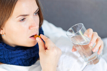 Influenza treatment or coronavirus . Flu-sick woman, wrapped in warm scarf and blanket , taking pills holding glass of water