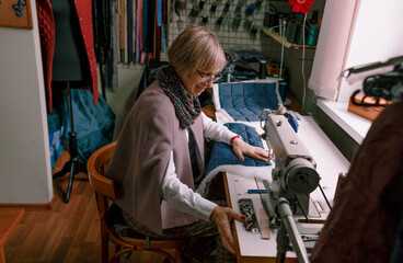 A female dressmaker uses a sewing machine to create custom-made clothes in a workshop. A female seamstress is busy sewing clothes in the workplace. Small business concept