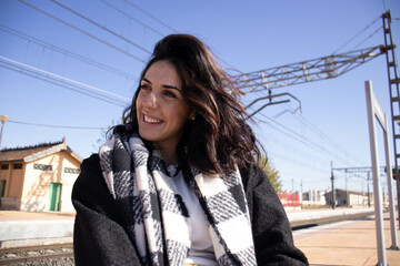 young brunette woman next to railroad arden with luggage, waiting for passenger train.