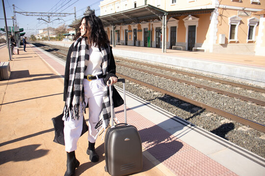 young brunette woman next to railroad arden with luggage, waiting for passenger train.