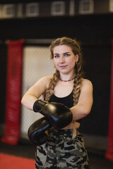 Young woman with braids prepares for a workout, she puts on boxing gloves and looks at a camera. 