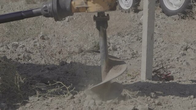 Tractor drill the ground. Drilling rig drills the ground, two workers help shovels. Machine drilling holes in the ground. Close up of auger. drilling a hole into the ground. Slow Motion 100 fps