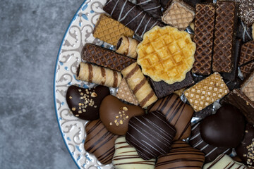 Different Christmas sweets, chocolate biscuits in plate and evergreen leaves on gray  table.