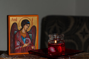 Hand painted orthodox icon during painting on piece of wood. Next to it is a red candle. Letters ΑΡΧ ΜΙΧΑИΛЪ means Archangels Michael.