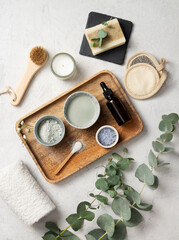 Fototapeta na wymiar the concept of organic cosmetics with clay, sea salt, soap, brush and eucalyptus branch in a wooden tray on a white textured background. Top view