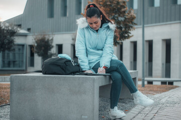 Muchacha joven estudiante sentada en un banco estudiando sus apuntes y libros en el campus...