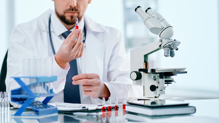 scientific researcher with an ampoule of vaccine, sitting at a laboratory table.