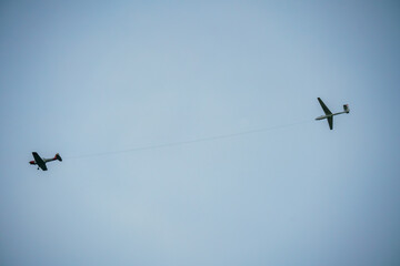 a British Navy 1950s De Havilland DHC-1 Chipmunk towing a glider aircraft flies low overhead in a winter sky
