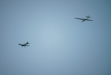 a British Navy 1950s De Havilland DHC-1 Chipmunk towing a glider aircraft flies low overhead in a winter sky