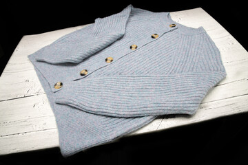 Light Blue Woollen Cardigan with tortoiseshell buttons round necked and laid out on a white wooden...