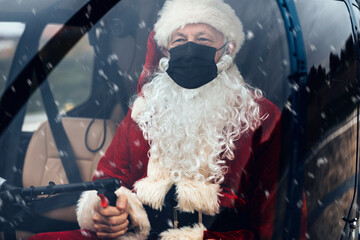 Obraz premium Santa Claus with protective face mask drives a heliopter and delivers gifts to children around the world.
