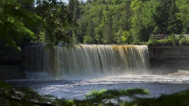 Medium View of Higher Falls of Tahquamenon Falls; rushing water drops into pool below, trees frame the banks; low angle.