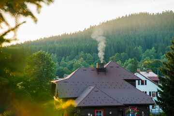 Smoking chimney of a rural cottage house in the woods on the background of mountains.