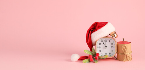 Alarm clock with Santa hat and candle on pink background with space for text