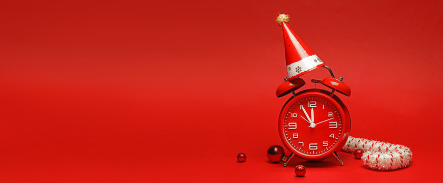 Alarm clock with party hat and Christmas decorations on red background with space for text