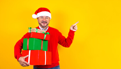 latin senior man holding Christmas presents with santa hat on yellow background in Mexico Latin America