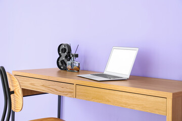Modern laptop, houseplant and reed diffuser on wooden table near color wall