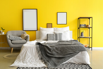 Interior of bright bedroom with blank frames and armchair