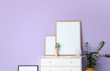 Wooden hand with sunglasses and blank frames on shelf near lilac wall