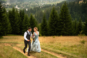 Wedding couple walks in the mountains. The groom leads the bride by the hand. The dress of the bride develops in the wind.