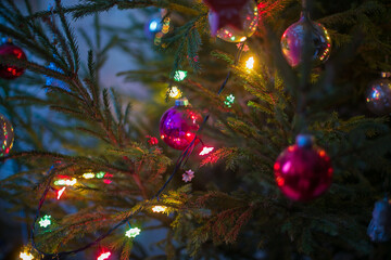 Obraz na płótnie Canvas Closeup of shiny balls and decorations hanging on fir tree branch against bokeh background with Christmas lights