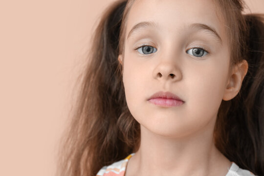Portrait of cute little girl with ponytails on beige background, closeup
