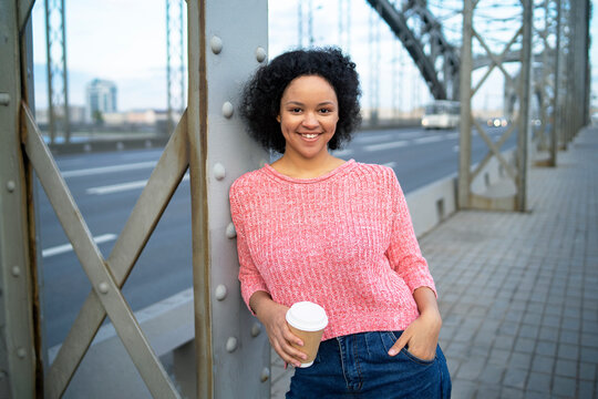 Happy dark-skinned woman walking in the city. Smiling African American Lifestyle holding a glass of coffee to go.