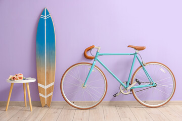 Table with flowers, surfboard and bicycle near lilac wall