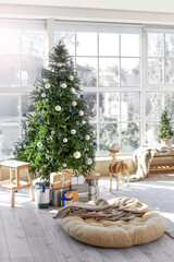 Beautiful decorated Christmas tree with gift boxes near big window in light living room