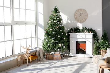 Interior of light living room with fireplace, decorated Christmas tree and wooden clock on light wall