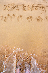 In den Sand geschriebener Schriftzug Teneriffa mit Textfreiraum und Füßen in einer Welle