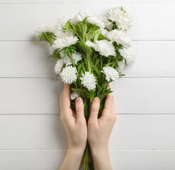 Female hands with bouquet of beautiful aster flowers on light wooden background, closeup