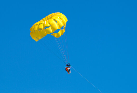 Yellow parasailing in blue sky with 3 people towed in Punta Cana