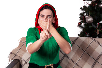 A handsome man dressed as Santa's helper sits on the couch with a surprised face. White background...