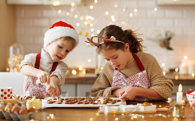 Happy children boy and girl smiling  while decorating Christmas gingerbreads in kitchen