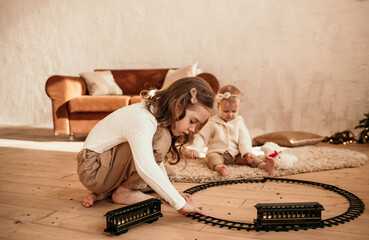 two sisters are sitting on a carpet and playing with a toy railroad and train