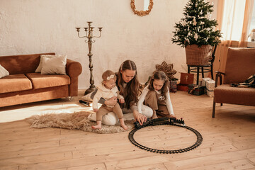 Fototapeta na wymiar loving mom plays with little daughters with a toy railroad on the floor in the room