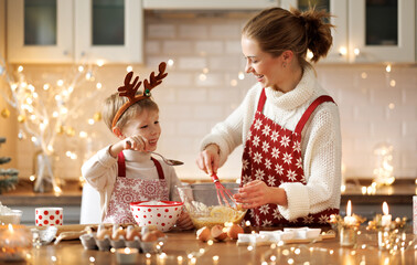 Cute little son boy helping mother to make dough for Christmas cookies in cozy kitchen at home