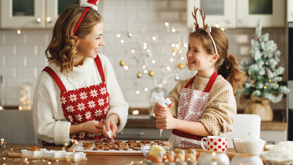 Happy family mother and girl daughter decorating Christmas gingerbread cookies after baking