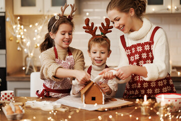 Happy family mother and two kids in xmas aprons decorating Christmas honey gingerbread house