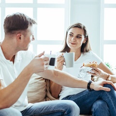 young couple drinks coffee sitting on the sofa in a new apartment.
