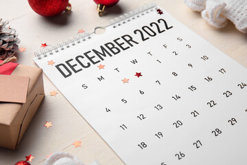 Paper calendar for December 2022, Christmas decor and confetti on light wooden table, closeup