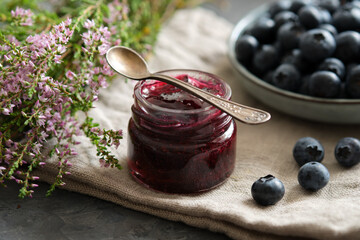 Small jar of blueberry jam and plate of fresh ripe blueberries on kitchen table.