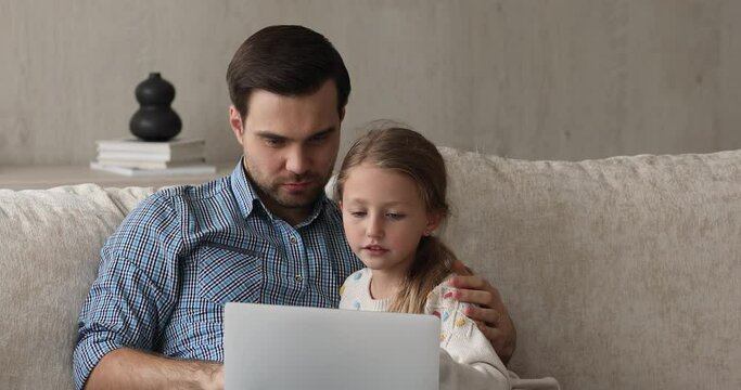 Online activity with dad. Loving father cuddle preteen child daughter using laptop on cozy couch playing funny web game using educational app. Happy single parent and little kid girl do shopping on pc