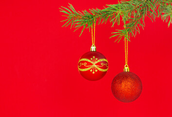 close-up of two beautiful red christmas baubles hanging on a spruce branch on a red background with copy space