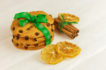 raisin cookies tied with green christmas ribbon, lemon slices and cinnamon on a white wooden table