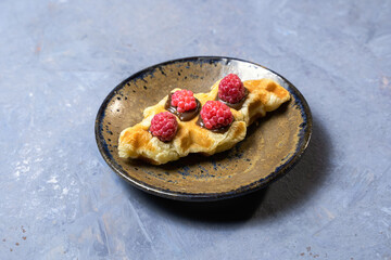 Croffles made of puff pastry, decorated with chocolate sauce and raspberries lies on a saucer. A popular Asian dessert. Close-up, copy space, top view. Culinary trend.
